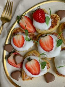 Plate of strawberry pancakes topped with cream and chocolate hearts, perfect for a sweet treat.